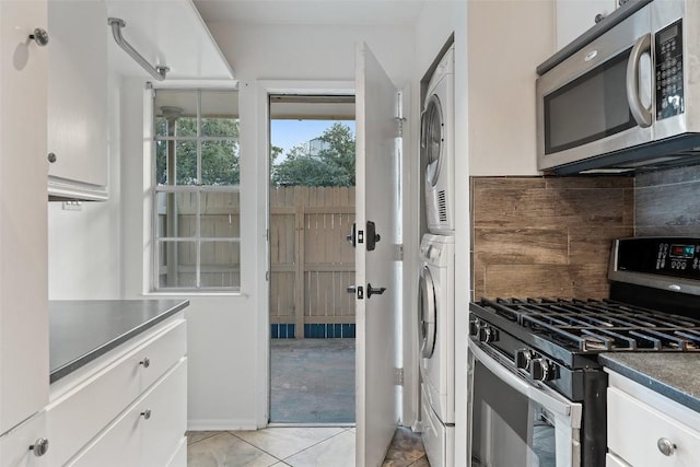 kitchen with stainless steel appliances, tasteful backsplash, white cabinets, stacked washer and dryer, and light tile patterned flooring