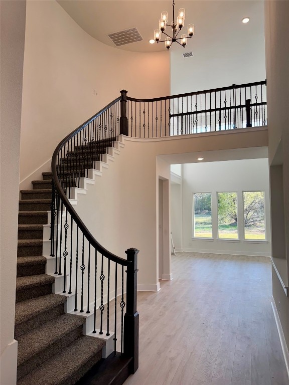 staircase with wood-type flooring, a towering ceiling, and an inviting chandelier