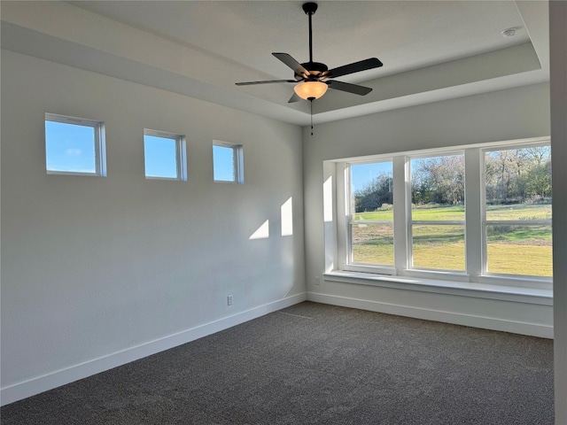 spare room featuring dark colored carpet, ceiling fan, and a raised ceiling