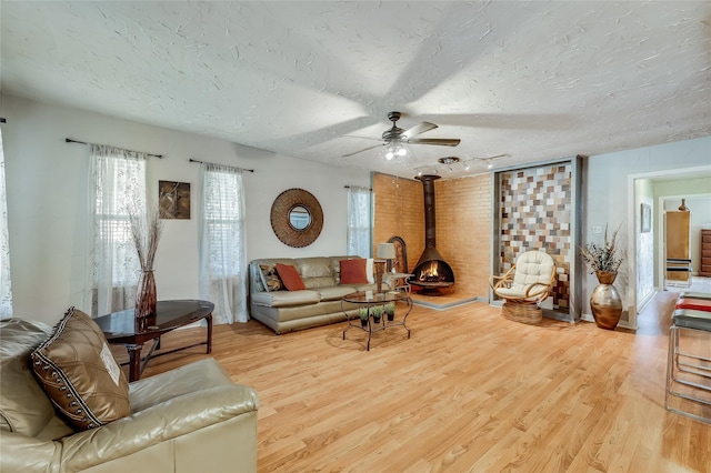 living room featuring ceiling fan, light hardwood / wood-style floors, a textured ceiling, and a wood stove