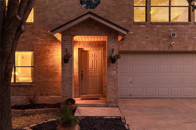 doorway to property featuring a garage, concrete driveway, and brick siding