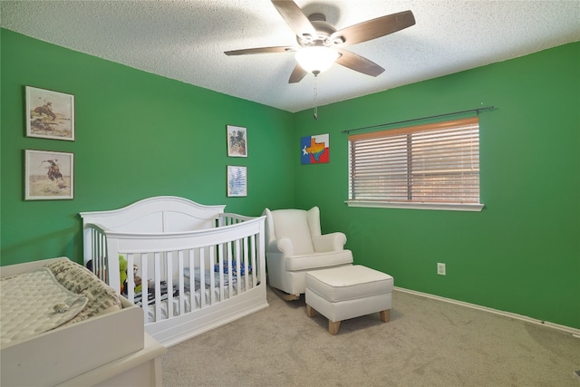 bedroom featuring a crib, ceiling fan, a textured ceiling, and light carpet