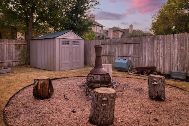 yard at dusk featuring a storage shed, an outbuilding, and a fenced backyard