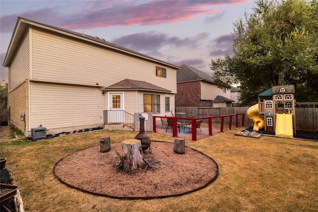 back house at dusk featuring a lawn, a playground, and a patio