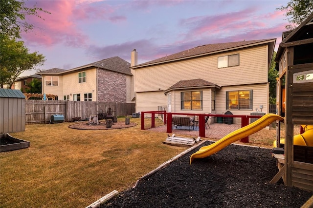 view of play area featuring a storage shed, a lawn, a patio, a fenced backyard, and an outbuilding