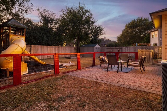 patio terrace at dusk featuring a playground and a storage shed