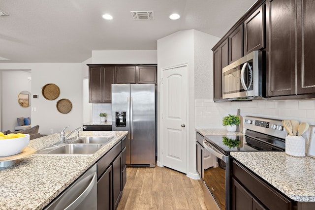 kitchen featuring sink, stainless steel appliances, backsplash, dark brown cabinets, and light wood-type flooring