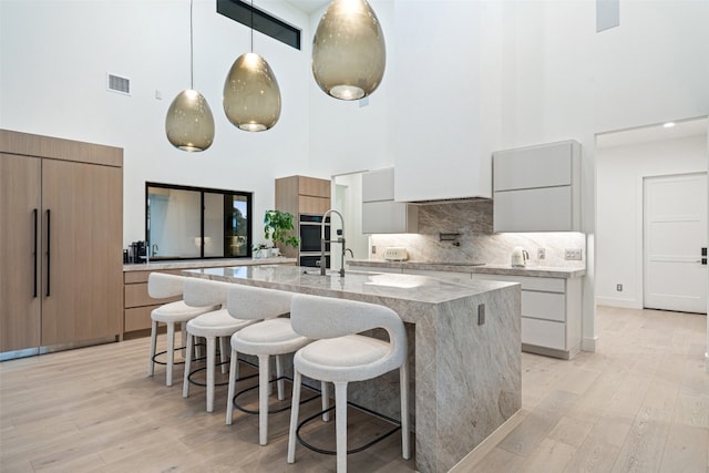 kitchen with decorative light fixtures, light hardwood / wood-style floors, a center island with sink, and a high ceiling