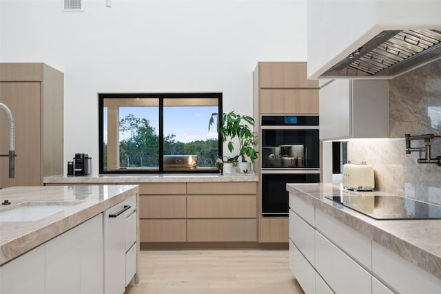 kitchen with backsplash, ventilation hood, black appliances, light hardwood / wood-style flooring, and sink