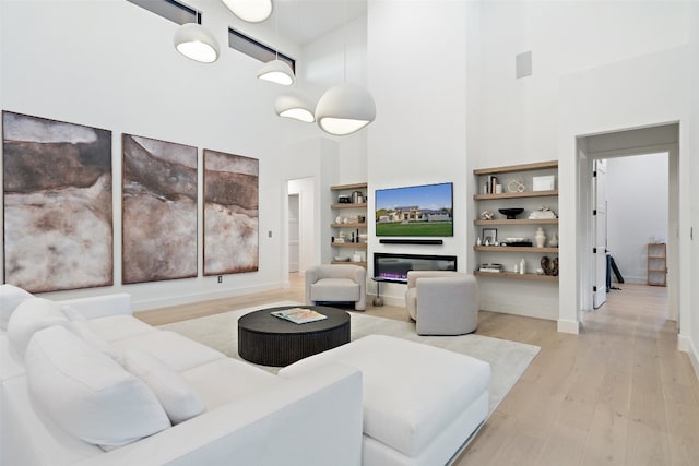 living room with a towering ceiling, built in shelves, and light wood-type flooring