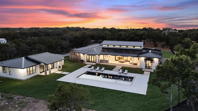 back house at dusk featuring a fire pit, a yard, and a patio area