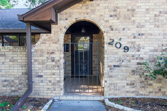 209 Simpson St, Schulenburg, TX 78956 - doorway to property with brick siding, a gate, and roof with shingles