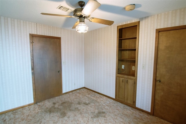 carpeted spare room with built in shelves, a textured ceiling, and ceiling fan