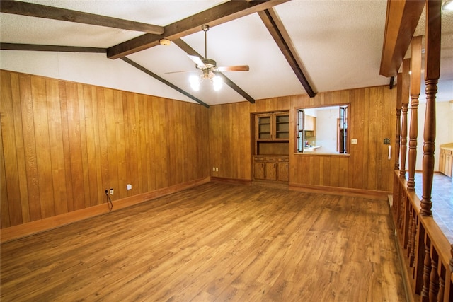 unfurnished living room featuring vaulted ceiling with beams, wood walls, ceiling fan, and hardwood / wood-style floors