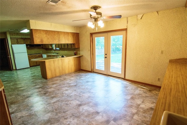 209 Simpson St, Schulenburg, TX 78956 - kitchen with freestanding refrigerator, a peninsula, french doors, a ceiling fan, and brown cabinetry