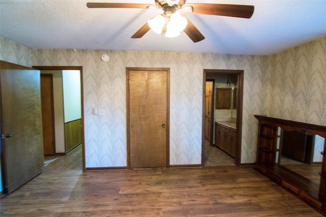 unfurnished bedroom with a textured ceiling, dark hardwood / wood-style floors, ceiling fan, and ensuite bathroom