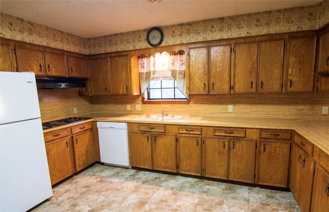209 Simpson St, Schulenburg, TX 78956 - kitchen featuring white appliances, under cabinet range hood, a sink, brown cabinets, and light countertops