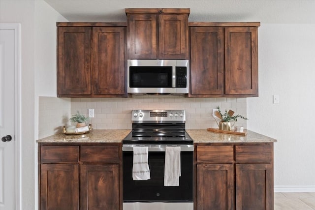 kitchen featuring light stone countertops, backsplash, appliances with stainless steel finishes, and light tile patterned floors