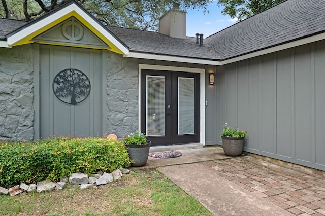 property entrance with french doors, roof with shingles, a chimney, a patio area, and stone siding