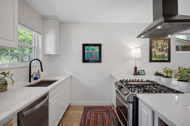 kitchen featuring island exhaust hood, stainless steel appliances, light countertops, white cabinetry, and a sink