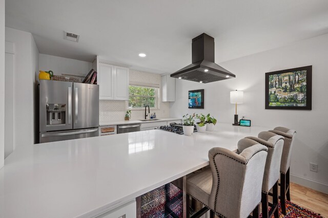 kitchen featuring sink, kitchen peninsula, island exhaust hood, white cabinetry, and stainless steel appliances