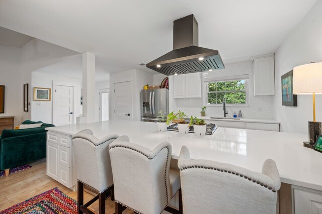 kitchen with light wood-type flooring, sink, white cabinets, stainless steel refrigerator with ice dispenser, and island exhaust hood