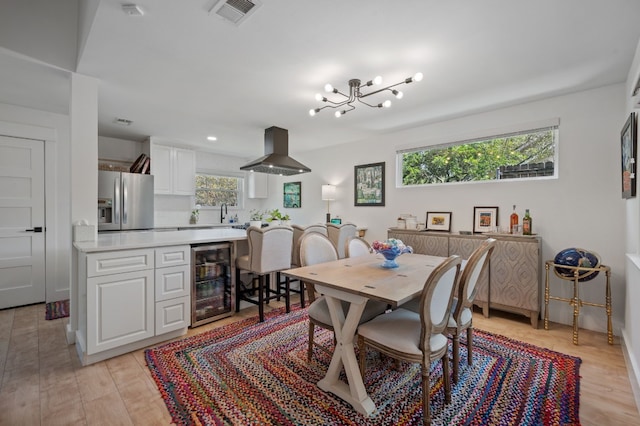 dining area featuring beverage cooler, light wood-style flooring, a chandelier, and visible vents