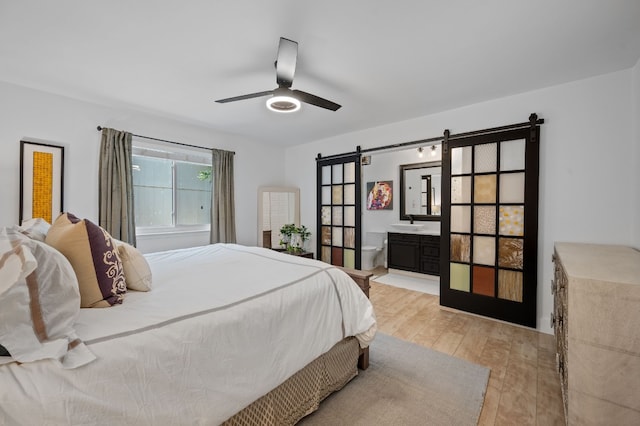 bedroom with a barn door, a ceiling fan, ensuite bath, light wood-style flooring, and a sink