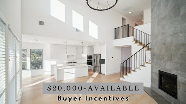 kitchen with a towering ceiling, appliances with stainless steel finishes, light wood-type flooring, a kitchen island, and white cabinetry