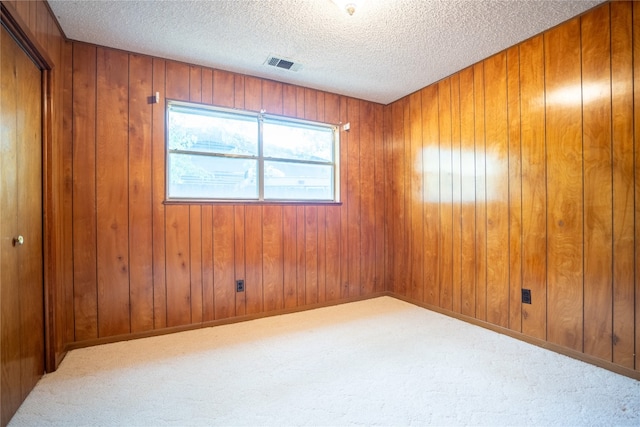 carpeted spare room featuring a textured ceiling and wooden walls