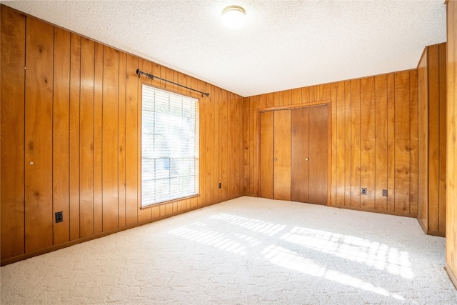 empty room with a textured ceiling, wood walls, and carpet