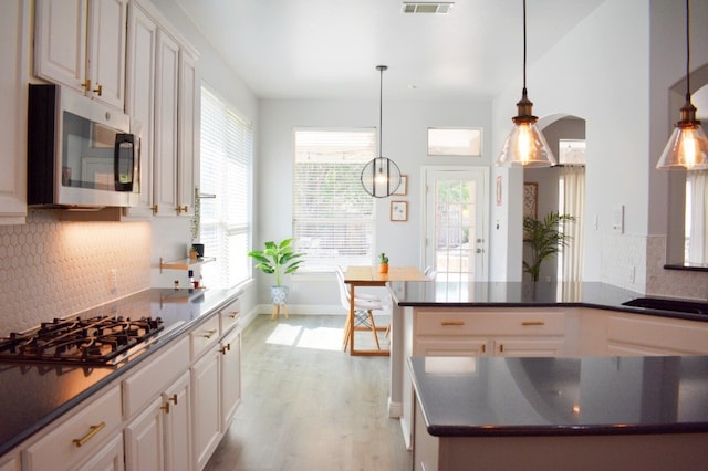 kitchen with appliances with stainless steel finishes, tasteful backsplash, sink, pendant lighting, and light hardwood / wood-style flooring