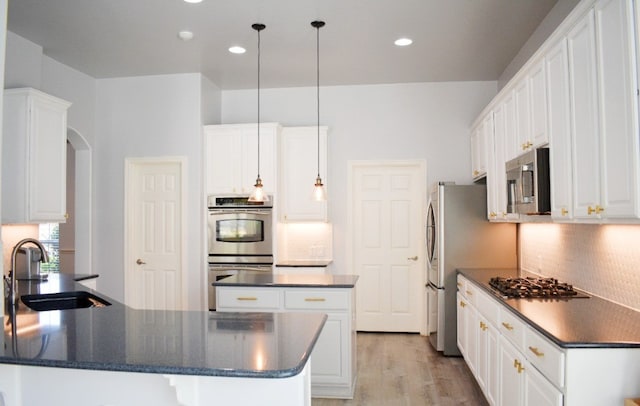 kitchen with appliances with stainless steel finishes, sink, decorative light fixtures, white cabinets, and light hardwood / wood-style floors