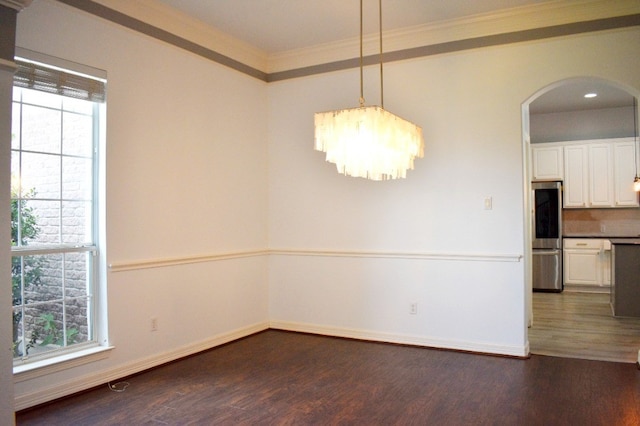 spare room featuring crown molding, dark wood-type flooring, a healthy amount of sunlight, and a notable chandelier