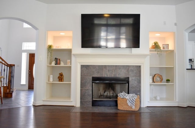 living room with built in shelves, dark wood-type flooring, a tile fireplace, and a high ceiling