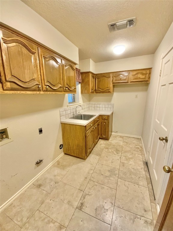 clothes washing area with washer hookup, a textured ceiling, electric dryer hookup, cabinets, and sink