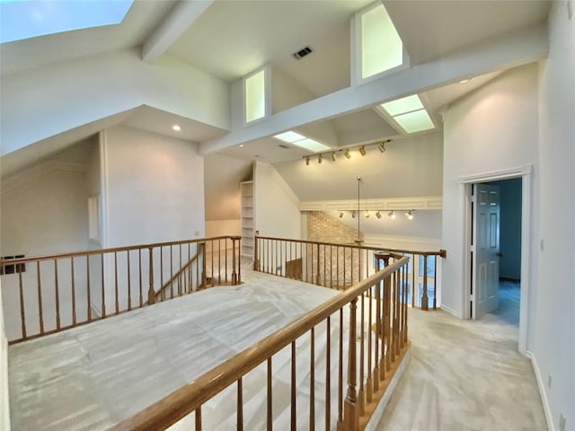 corridor with light carpet, a skylight, beam ceiling, and high vaulted ceiling