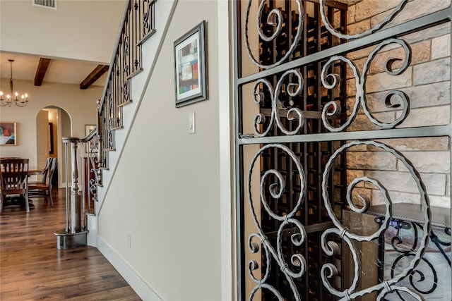 stairs with wood-type flooring, beam ceiling, and a chandelier