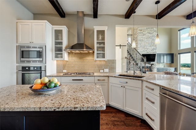 kitchen featuring a barn door, stainless steel appliances, beam ceiling, sink, and wall chimney range hood