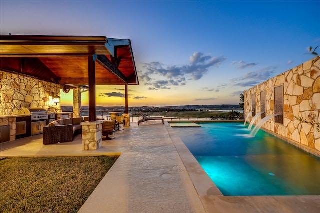 pool at dusk featuring area for grilling, an outdoor kitchen, a patio area, and pool water feature