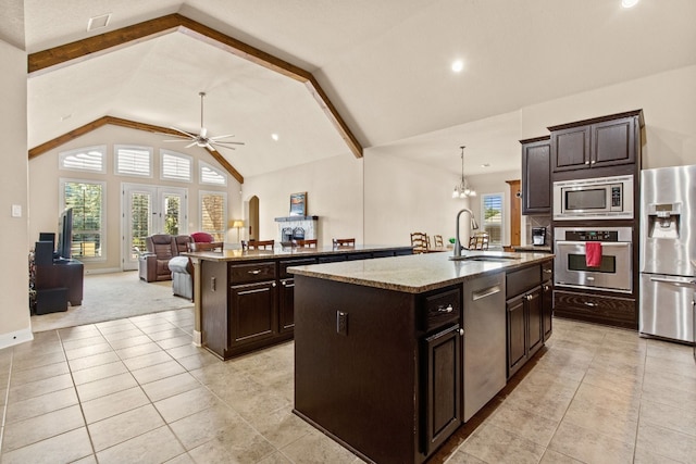 kitchen with an island with sink, hanging light fixtures, sink, appliances with stainless steel finishes, and lofted ceiling with beams