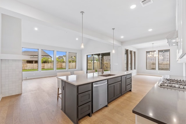 kitchen with appliances with stainless steel finishes, sink, light wood-type flooring, pendant lighting, and an island with sink