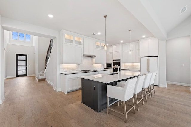 kitchen with white cabinets, decorative light fixtures, a center island with sink, and light hardwood / wood-style flooring