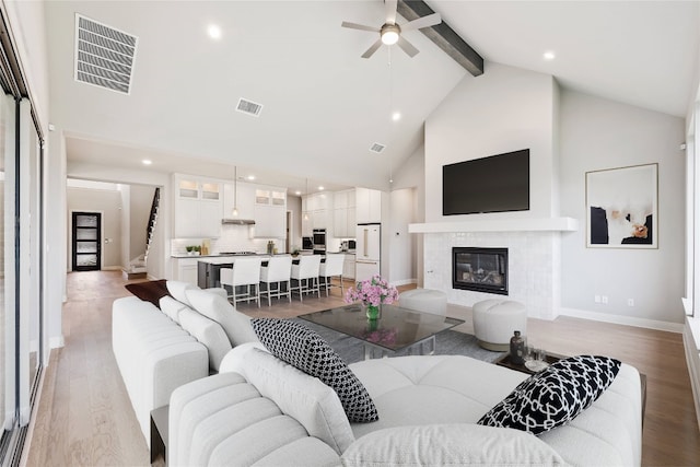 living room featuring high vaulted ceiling, light hardwood / wood-style flooring, ceiling fan, a fireplace, and beamed ceiling