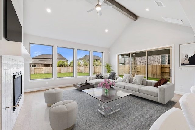 living room with ceiling fan, a tiled fireplace, light wood-type flooring, high vaulted ceiling, and beamed ceiling