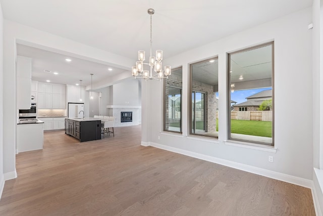 unfurnished dining area with a fireplace, sink, light hardwood / wood-style flooring, and a chandelier