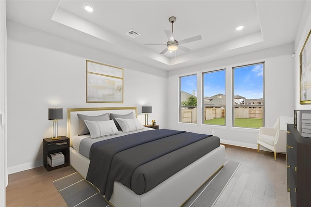 bedroom with ceiling fan, wood-type flooring, and a tray ceiling