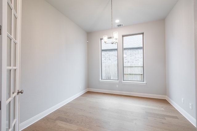 unfurnished room with plenty of natural light, a chandelier, and light hardwood / wood-style floors