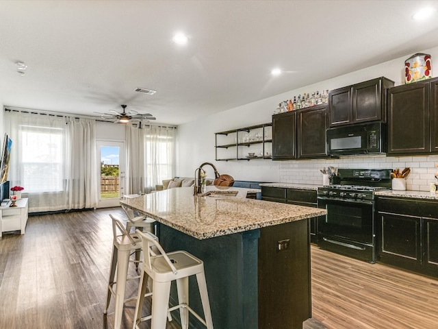 kitchen with ceiling fan, sink, light hardwood / wood-style flooring, a kitchen island with sink, and black appliances