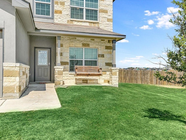 property entrance with a yard, fence, and stone siding